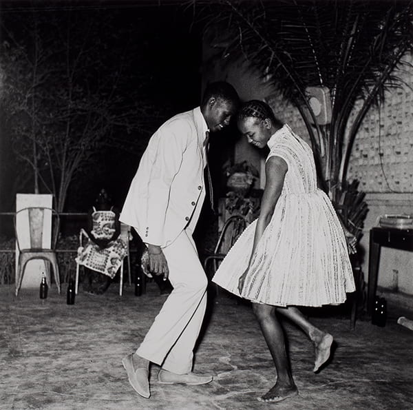 Black and white photo of two people dancing with their heads tilting towards each other.